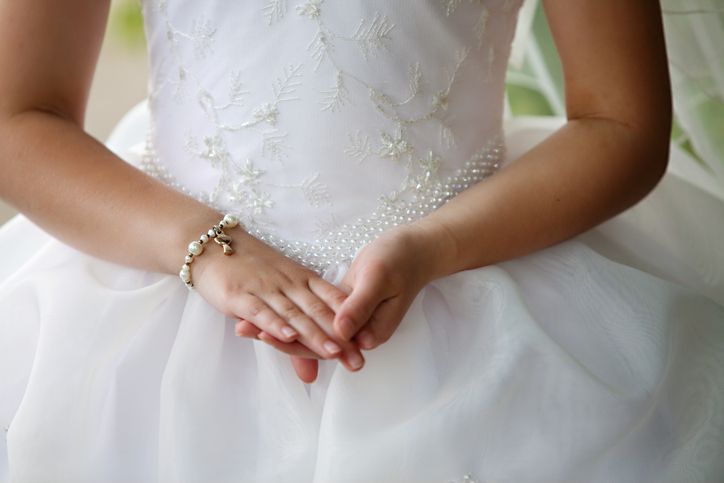 Una bambina con un vestito bianco indossa un braccialetto al polso.