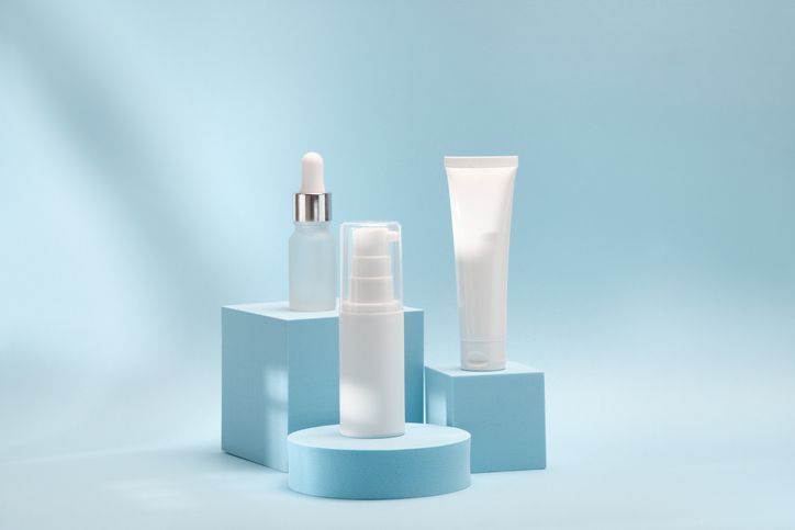 Tre bottiglie di cosmetici sono appoggiate su cubi blu su uno sfondo blu.