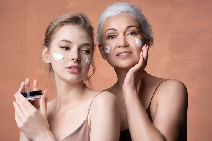 Una giovane donna e una donna anziana si stanno applicando la crema sul viso.