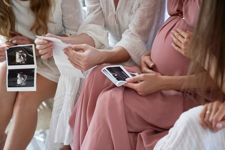 Un gruppo di donne incinte sono sedute una accanto all'altra e tengono in mano le immagini dell'ecografia.