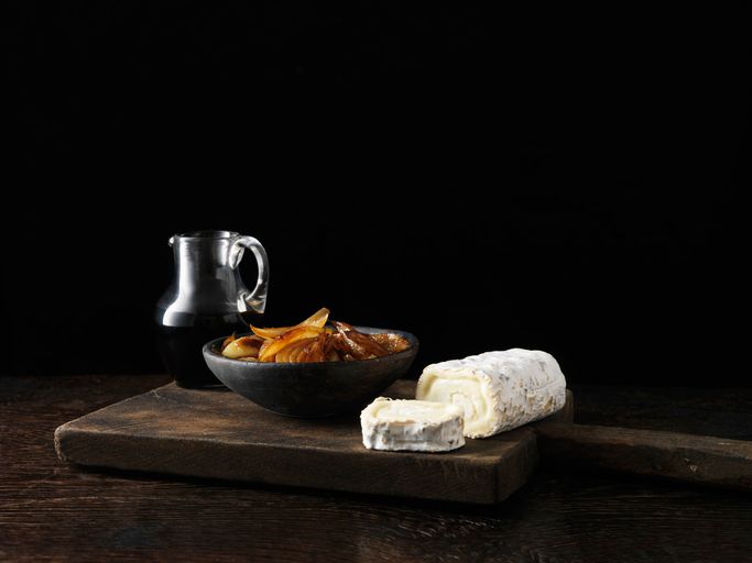 C'è una ciotola di frutta secca e un pezzo di formaggio su un tagliere.