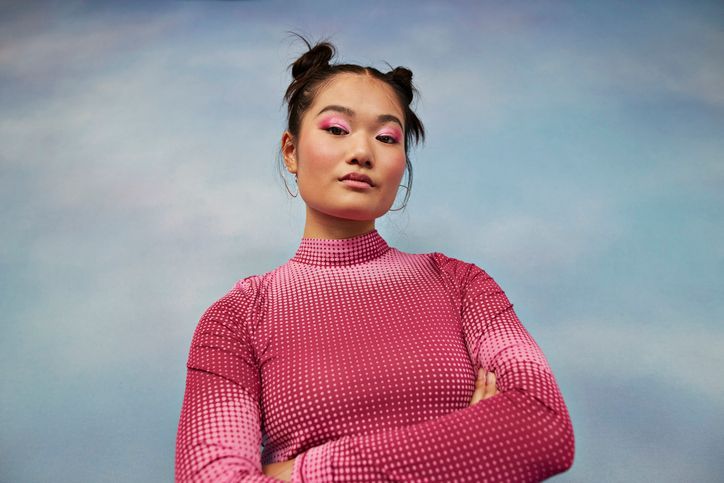 Una donna con un maglione rosa è in piedi con le braccia incrociate.