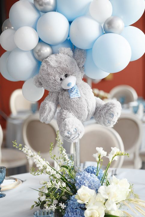 Un orsacchiotto è seduto su un tavolo con palloncini e fiori.