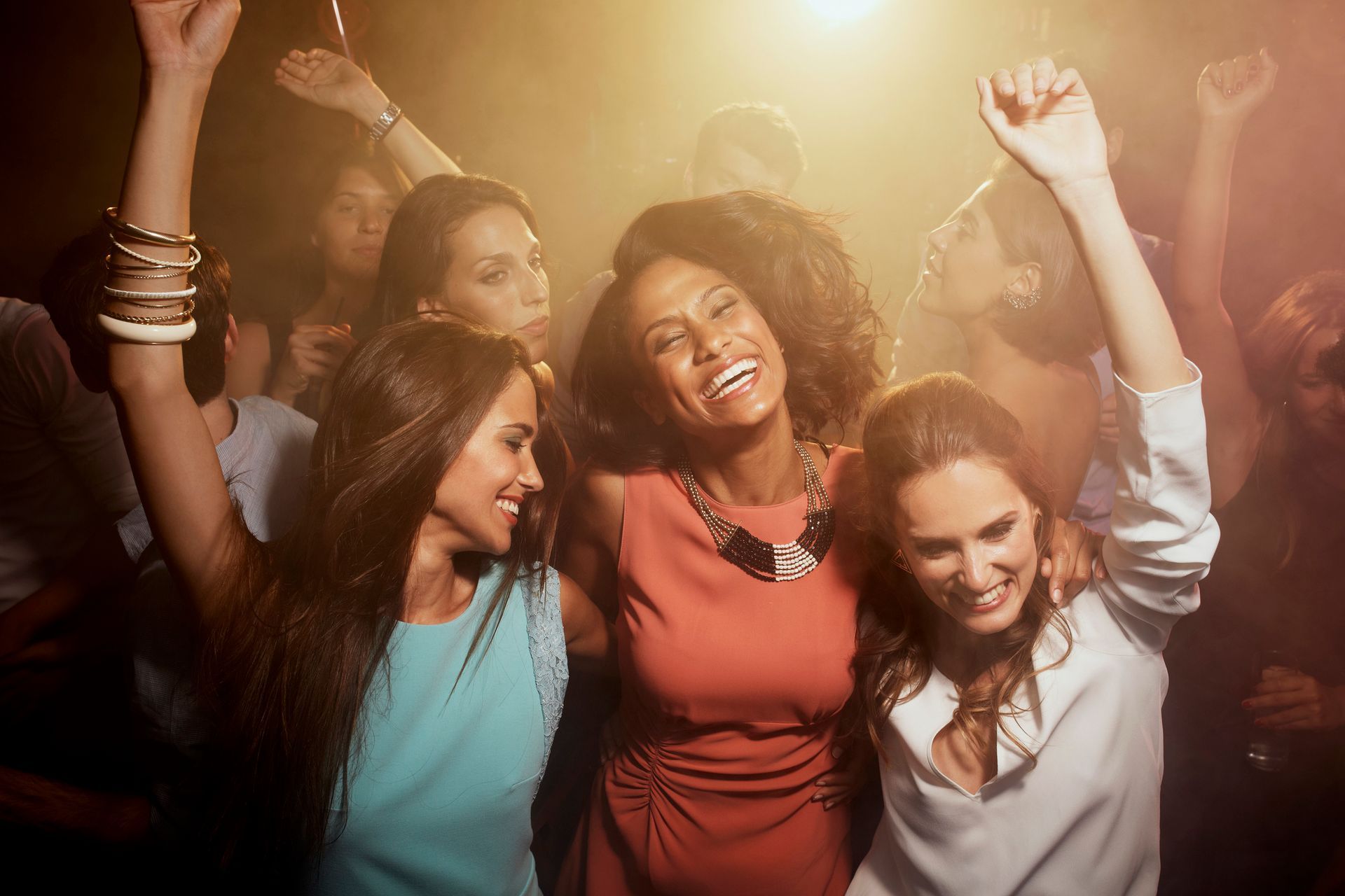 Un gruppo di donne balla in una discoteca con le braccia alzate.