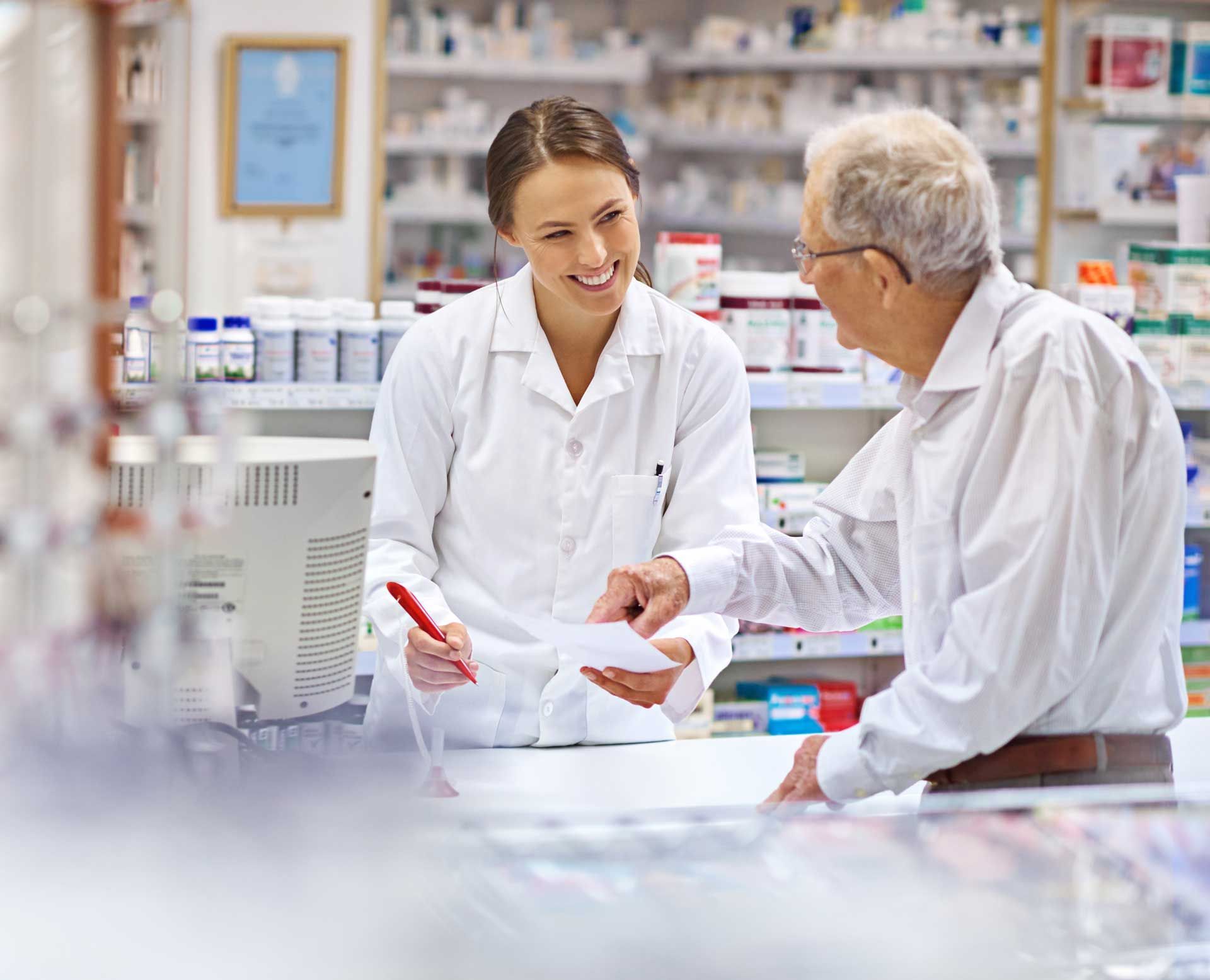 A female pharmacist is talking to an older man in a pharmacy.