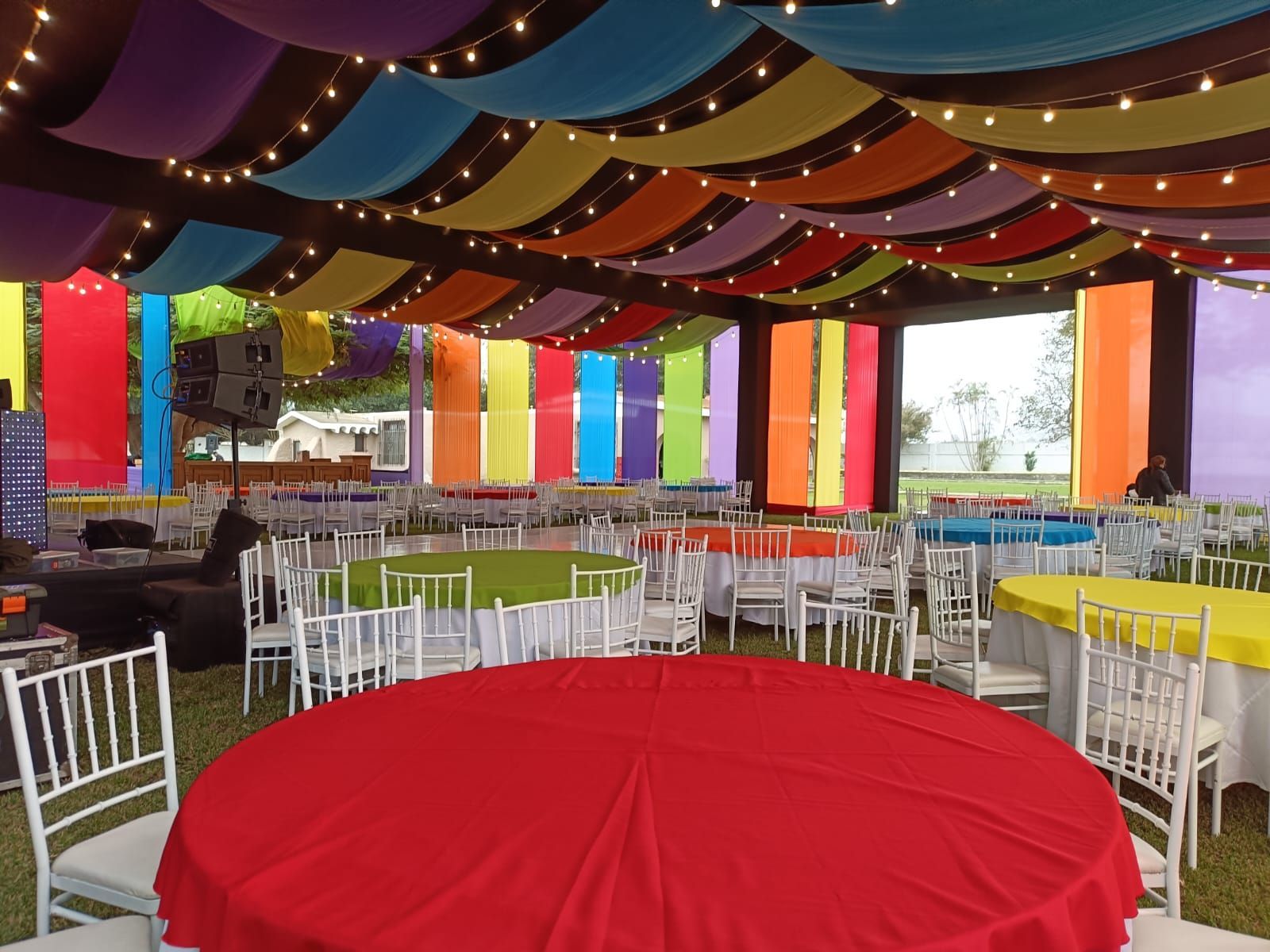Carpa colorida para eventos con filas de sillas y mesas blancas, mesa redonda roja en primer plano.