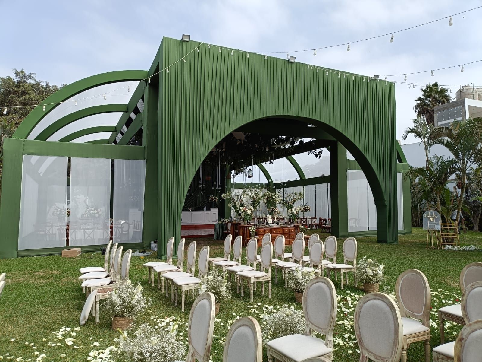 Outdoor event stage with green draped arch and rows of white chairs on a lawn