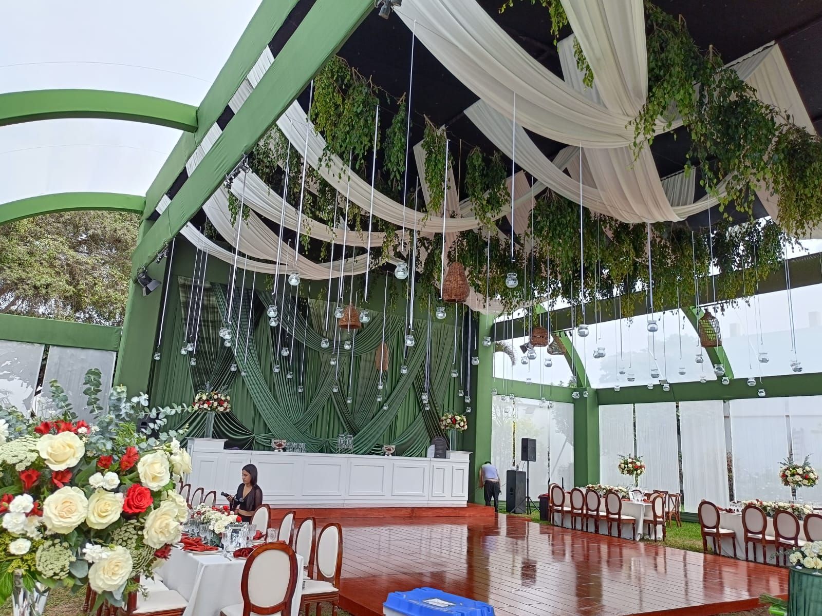 Elegante espacio para eventos en interiores con arcos verdes, cortinas blancas colgantes, arreglos florales