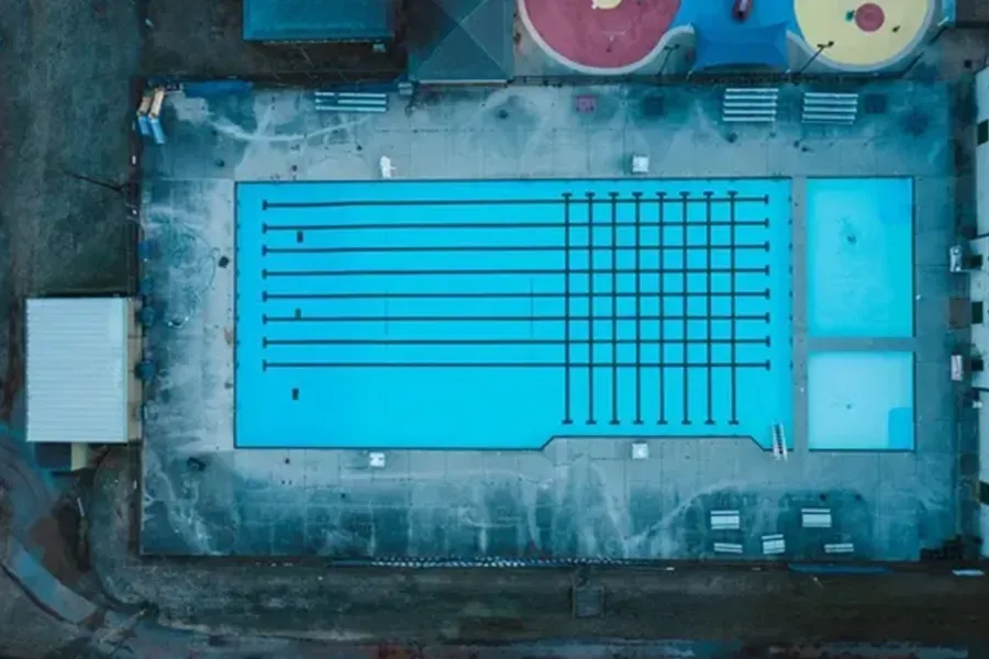 Aerial view of a turquoise outdoor swimming pool with lane markings and surrounding deck.