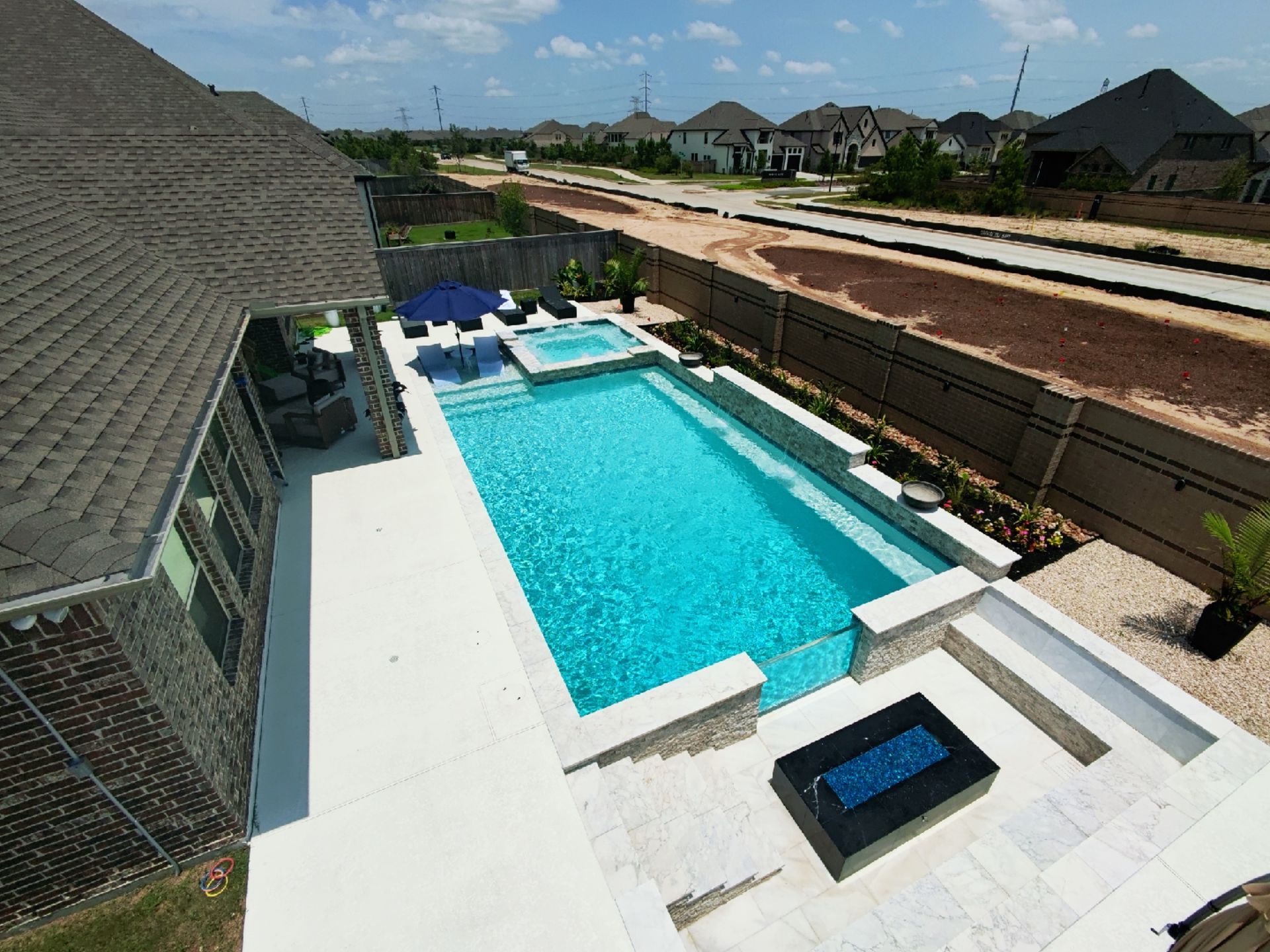 Backyard pool with loungers, umbrella, and lush tropical greenery under cloudy skies