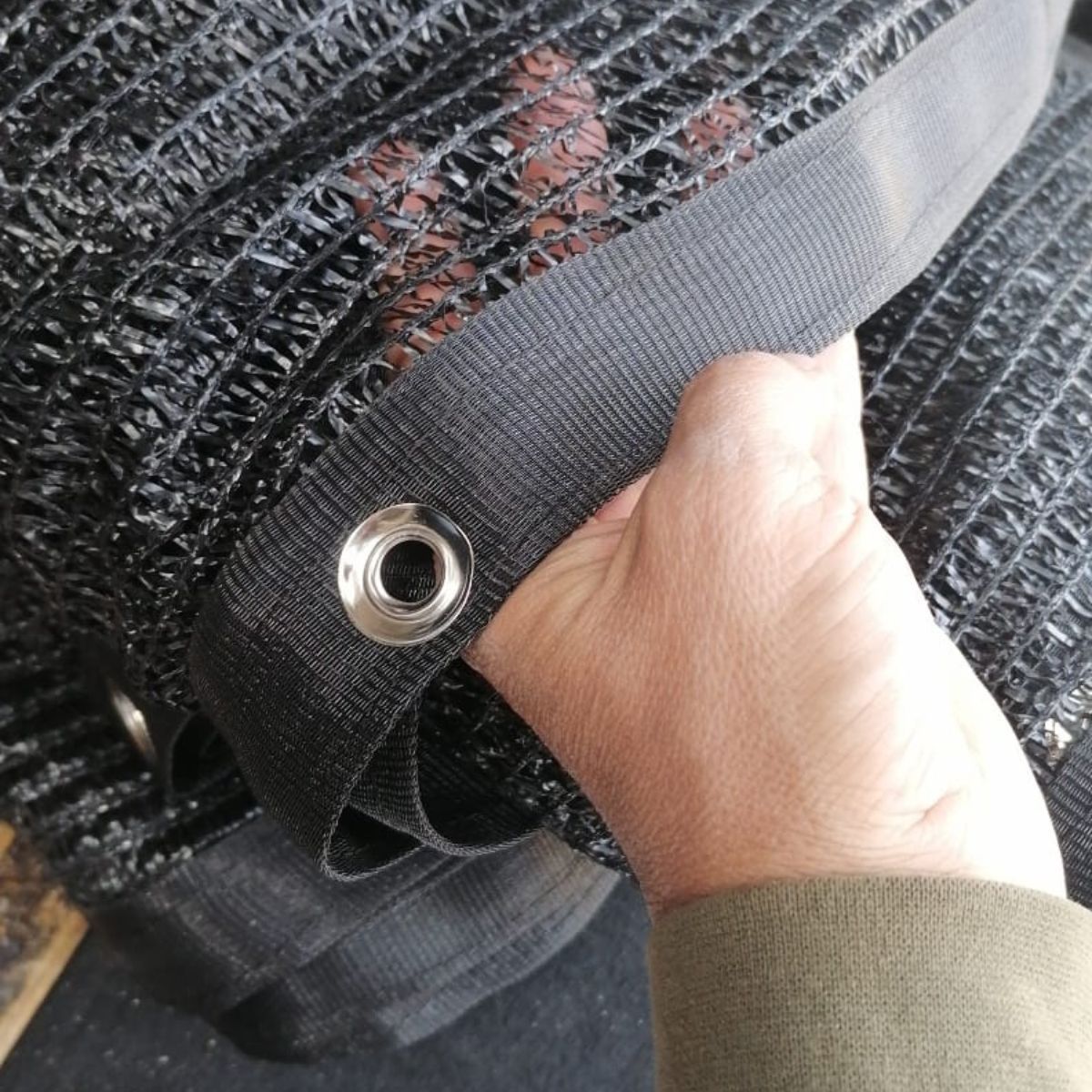 Hand gripping a black mesh fabric with a metal grommet and strap clip inside a bag or seat netting