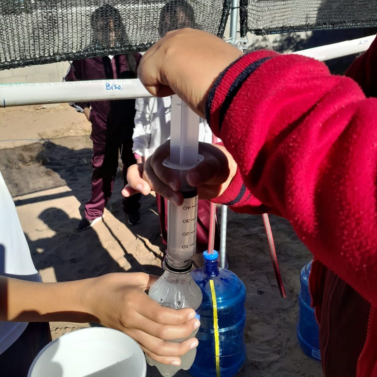 Hands using a hand pump to fill a bottle with water outdoors