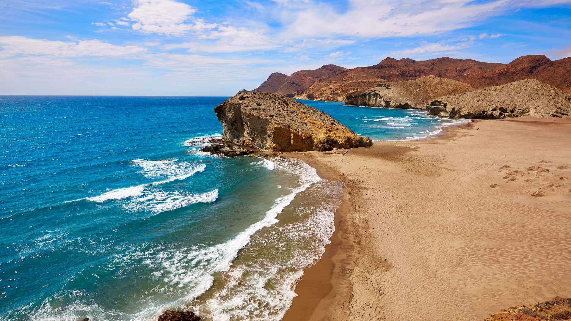 Sandy beach with turquoise waves, rocky cliffs, and a bright blue sea under clear skies