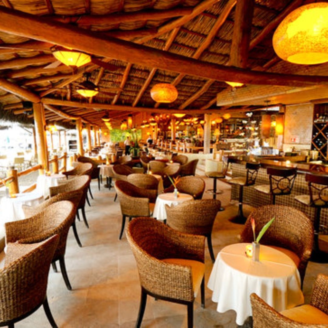 A restaurant with wicker chairs and tables under a thatched roof