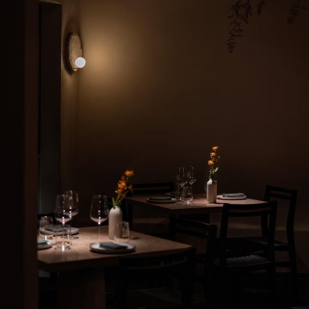 A dark room with tables and chairs and a light on the wall