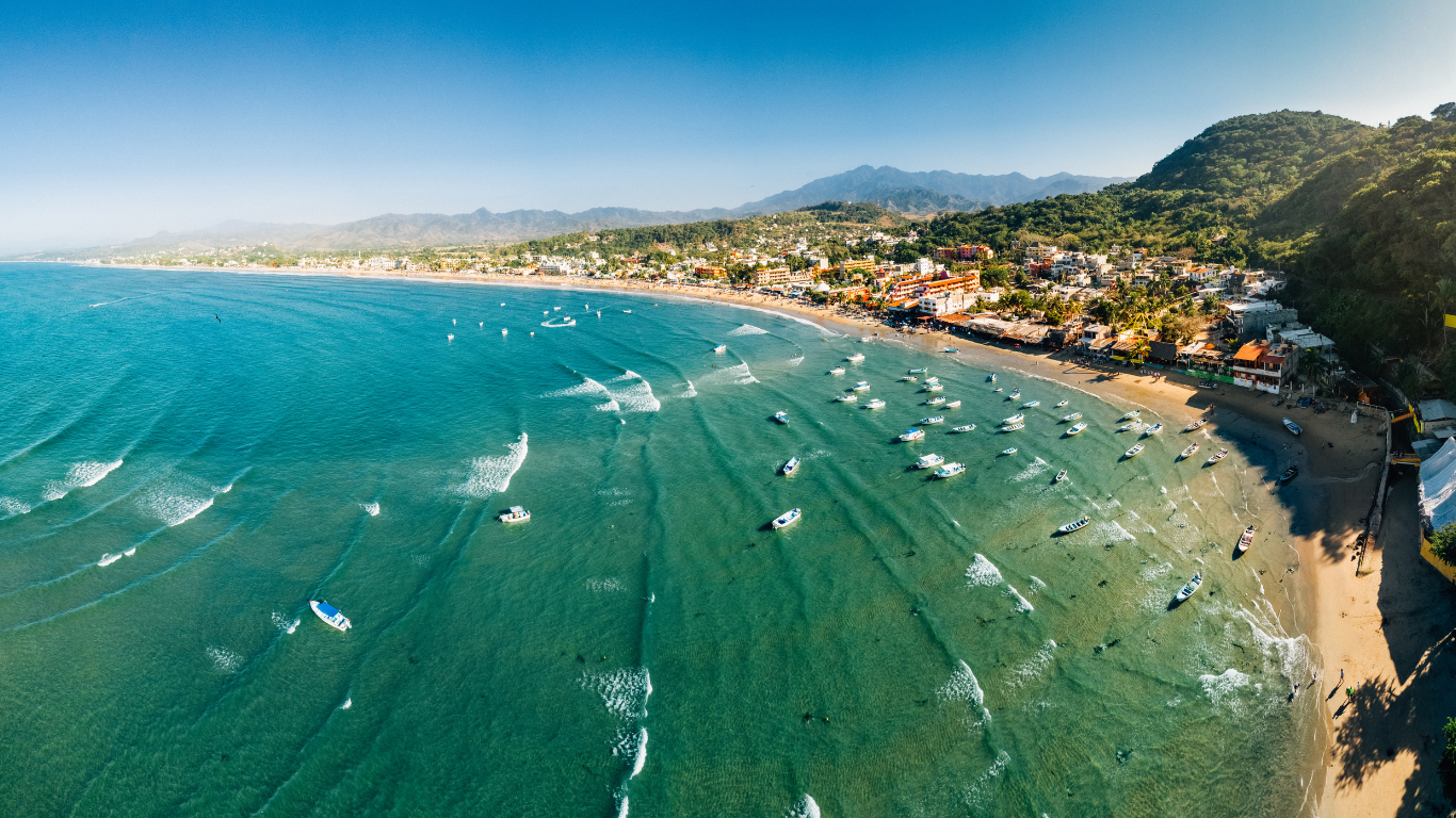 An aerial view of a beach with a lot of surfers in the water.
