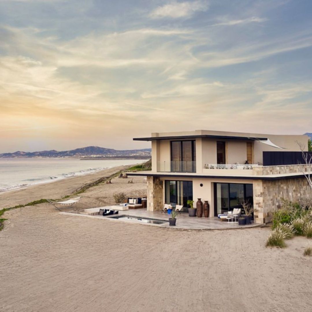 A large house is sitting on top of a sandy beach next to the ocean.