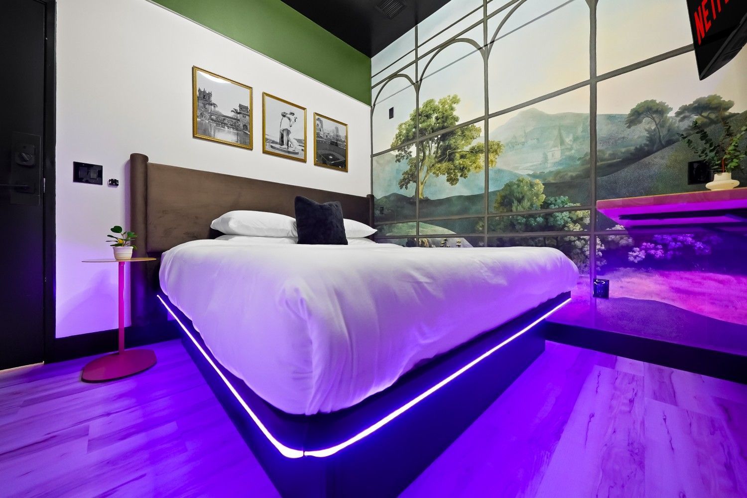 Modern bedroom with a bed lit by purple LED lights, framed wall art, and a scenic mural window view