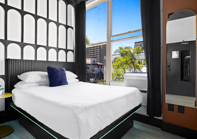 Modern hotel room with a white bed, blue pillow, tall window, and dark curtains