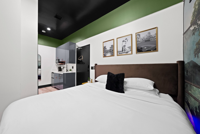Modern bedroom with white bedding, dark wood headboard, green ceiling, and framed art on the wall