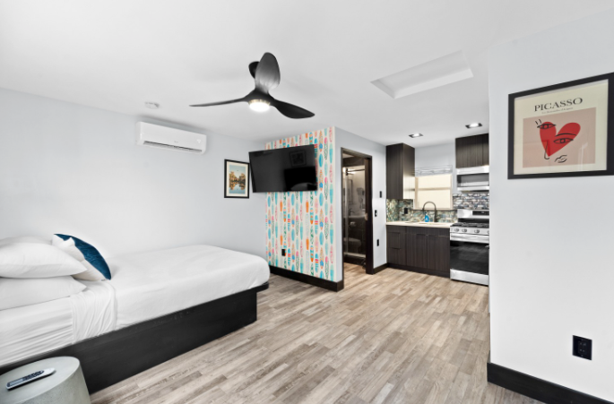 Modern bedroom with bed, ceiling fan, TV, patterned partition, and kitchenette area