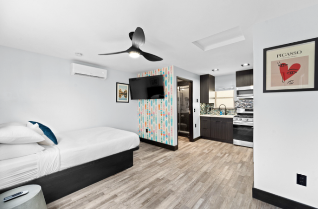 Modern bedroom with bed, ceiling fan, TV, patterned partition, and kitchenette area