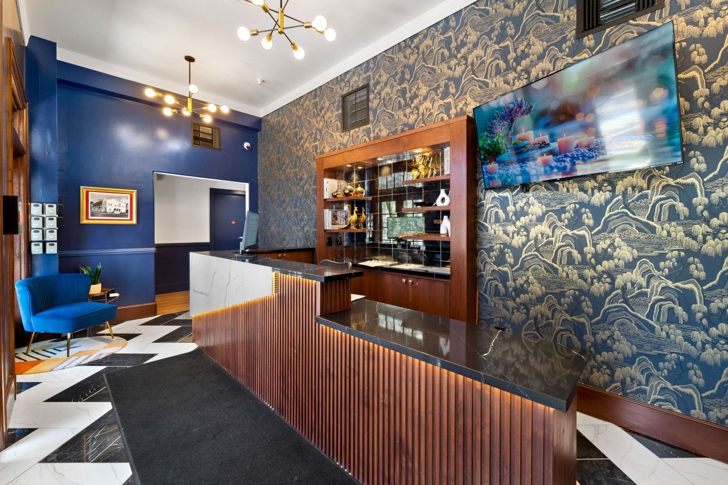 Stylish hotel lobby with a wood reception desk, blue patterned wallpaper, and geometric black-and-white floor