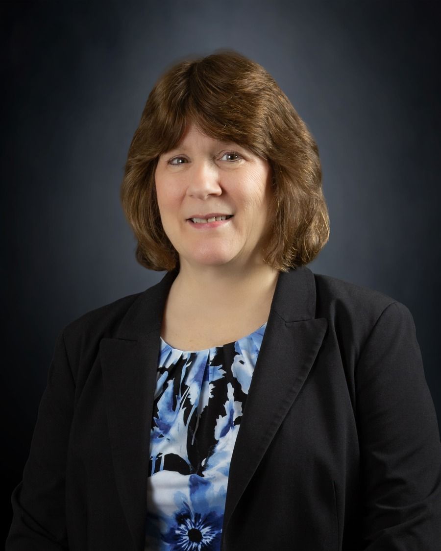 Studio portrait of a woman in a black blazer and blue patterned blouse against a dark background