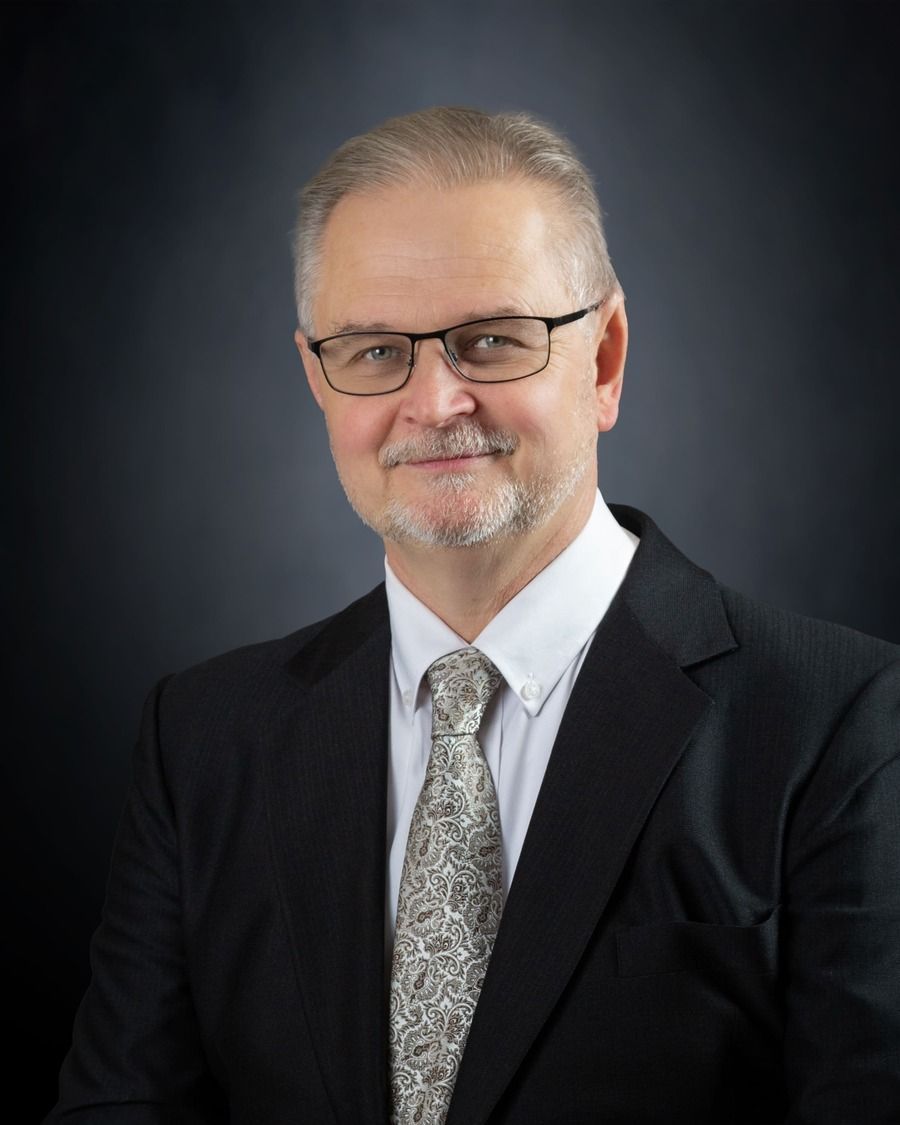 Portrait of a man in a dark suit and patterned tie against a dark studio background