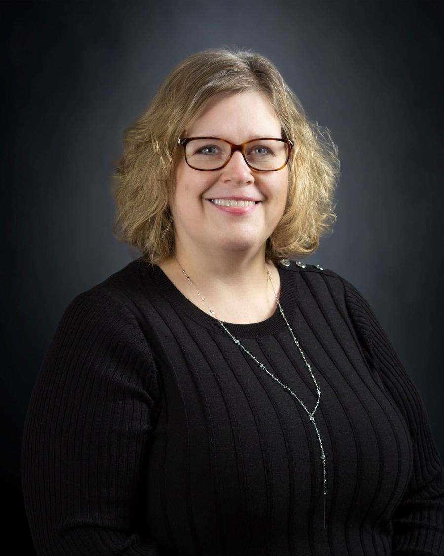Smiling person in glasses wearing a black sweater against a dark studio background