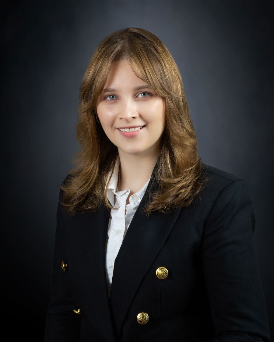 Studio portrait of a smiling woman in a black blazer with gold buttons against a dark background