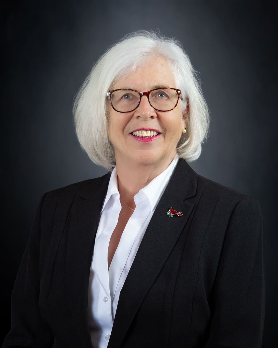 Portrait of a smiling person in a black blazer and white shirt against a dark background