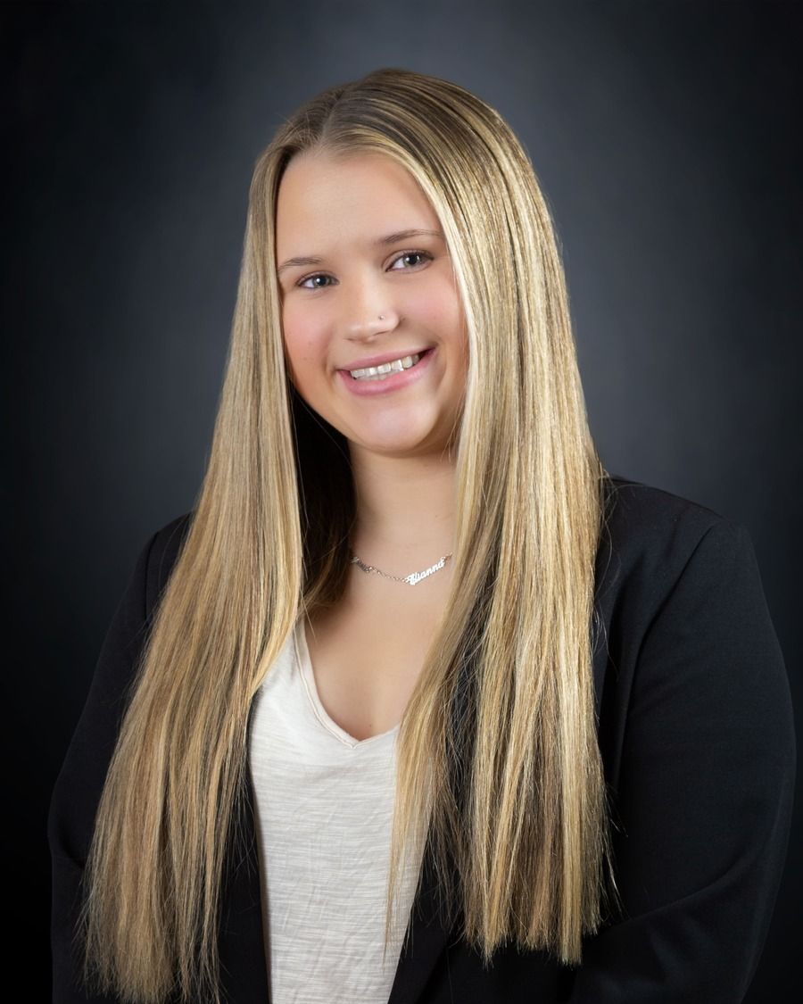 Smiling woman with long blonde braids wearing a black blazer against a dark studio background