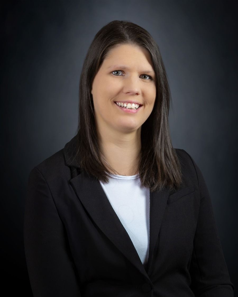 Smiling professional in a black blazer against a dark studio background.