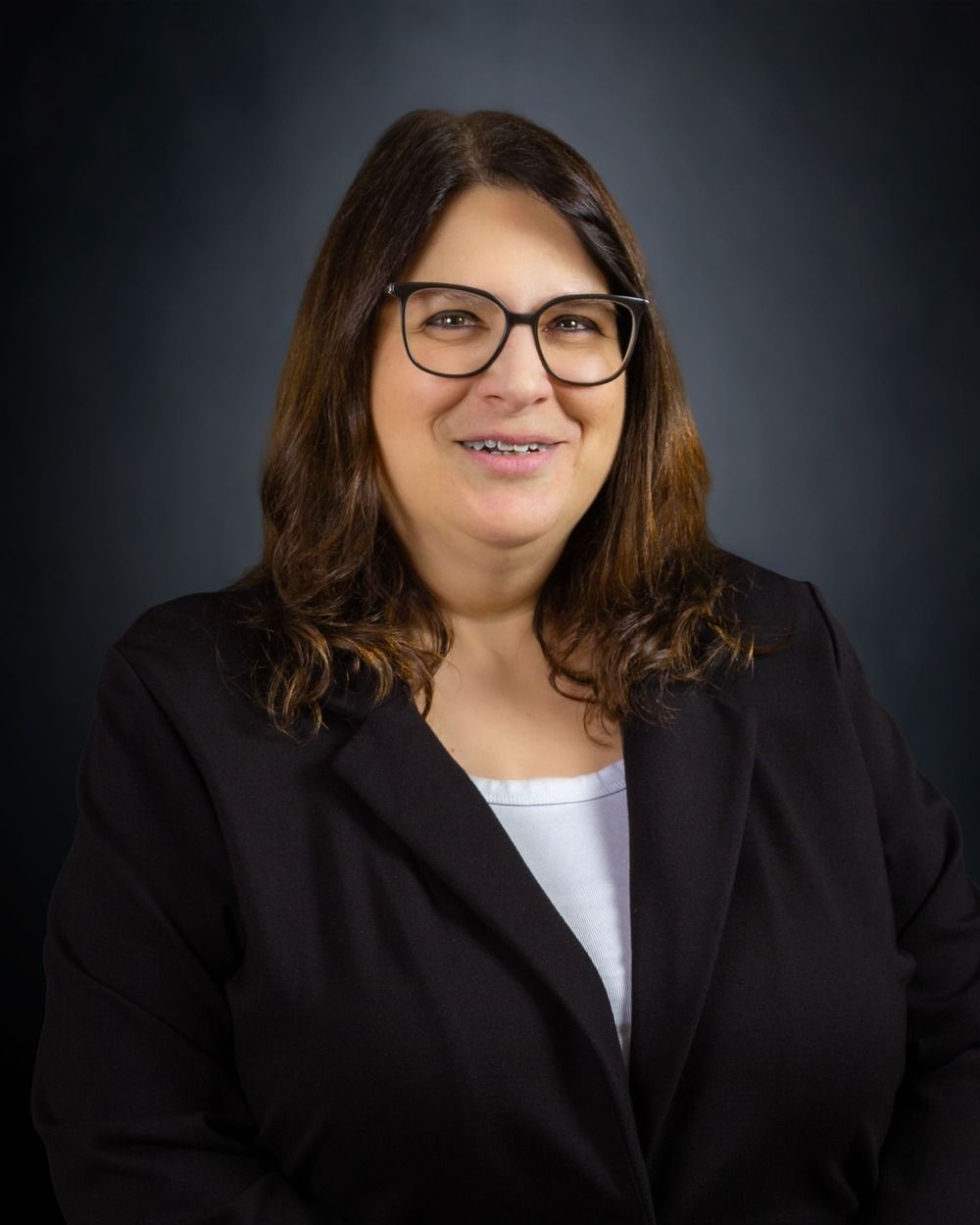 Portrait of a smiling woman in glasses wearing a black blazer against a dark background