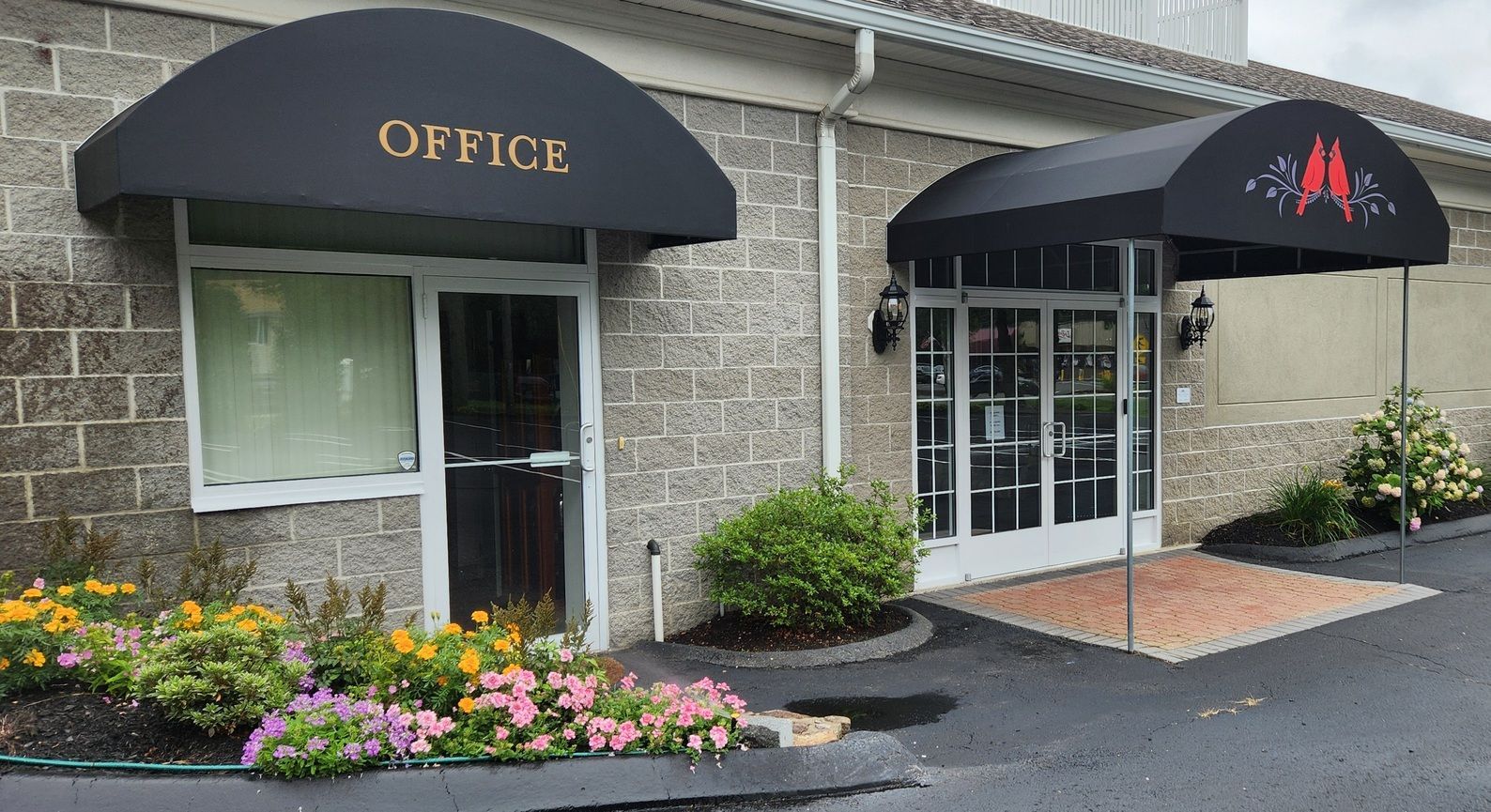 Office entrance with black awnings, stone facade, and flower beds by the doorway