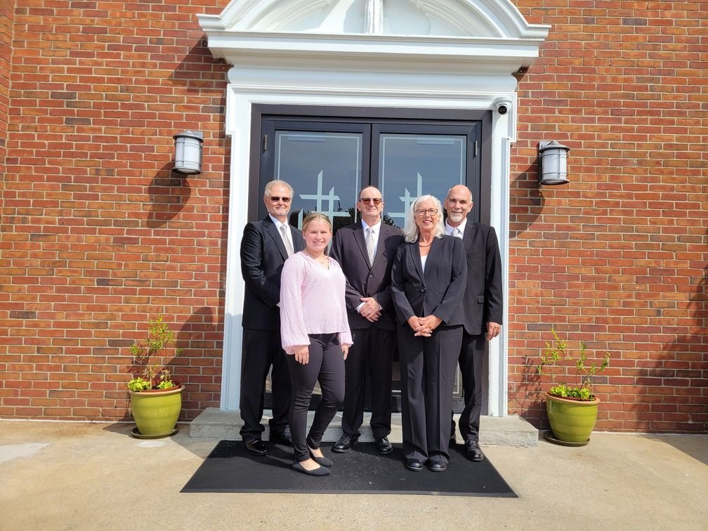 Six people standing outside a brick building entrance, posing together in formal attire.