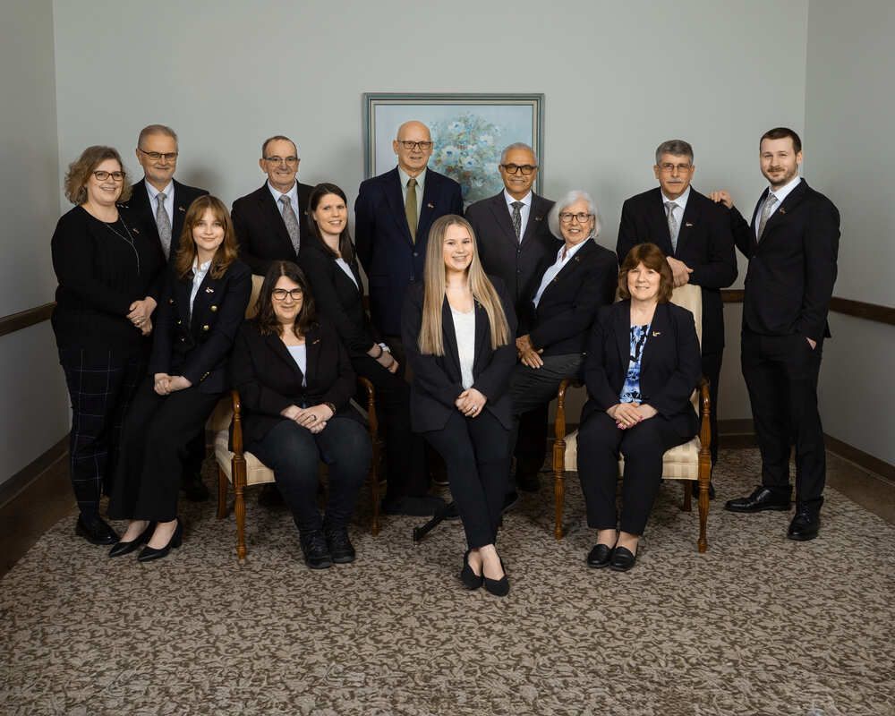 Group of professionally dressed people posing for a formal team photo indoors in an office setting.