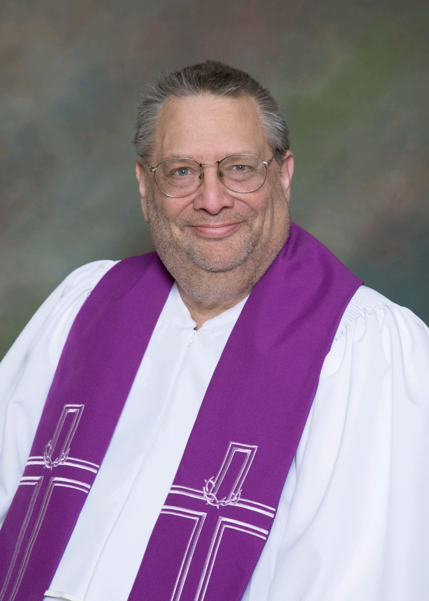 Clergyman in white robe and purple stole posing against a studio backdrop