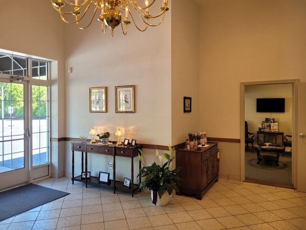 Bright hotel lobby with chandelier, side tables, potted plant, and glass doors to outside