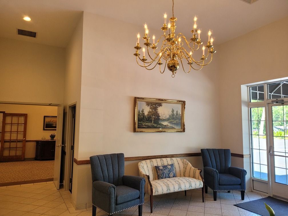 Elegant lobby with chandelier, framed art, blue armchairs, and glass doors opening to greenery