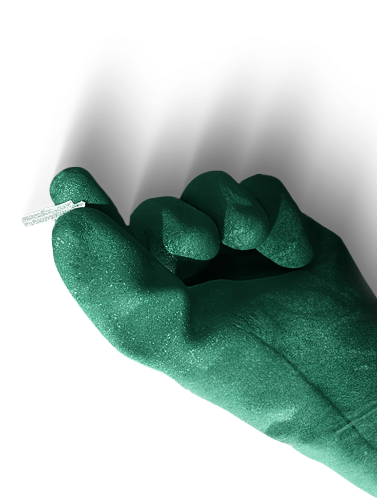Mão com luva verde segurando um pequeno fio branco contra um fundo liso.