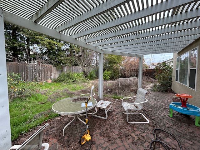 Covered backyard patio with table, chairs, and children’s toys on a dirt floor beneath a slatted roof.