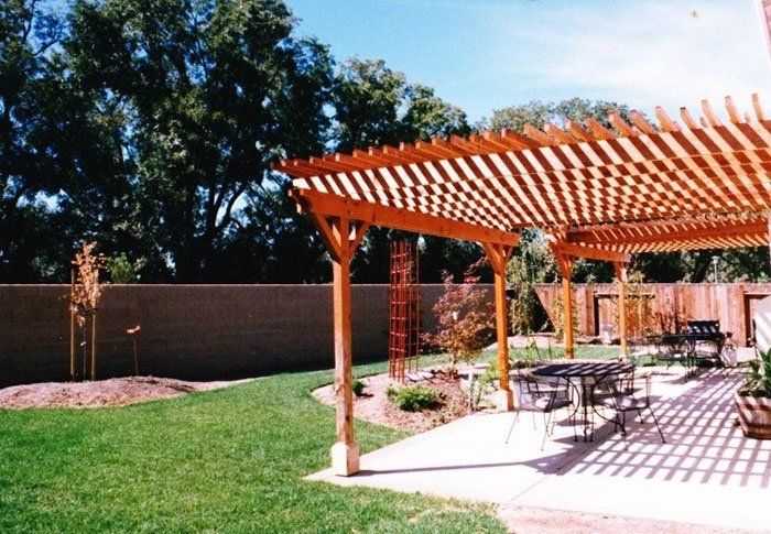 Backyard patio with a wooden pergola, table and chairs, brick wall, and green lawn in sunlight