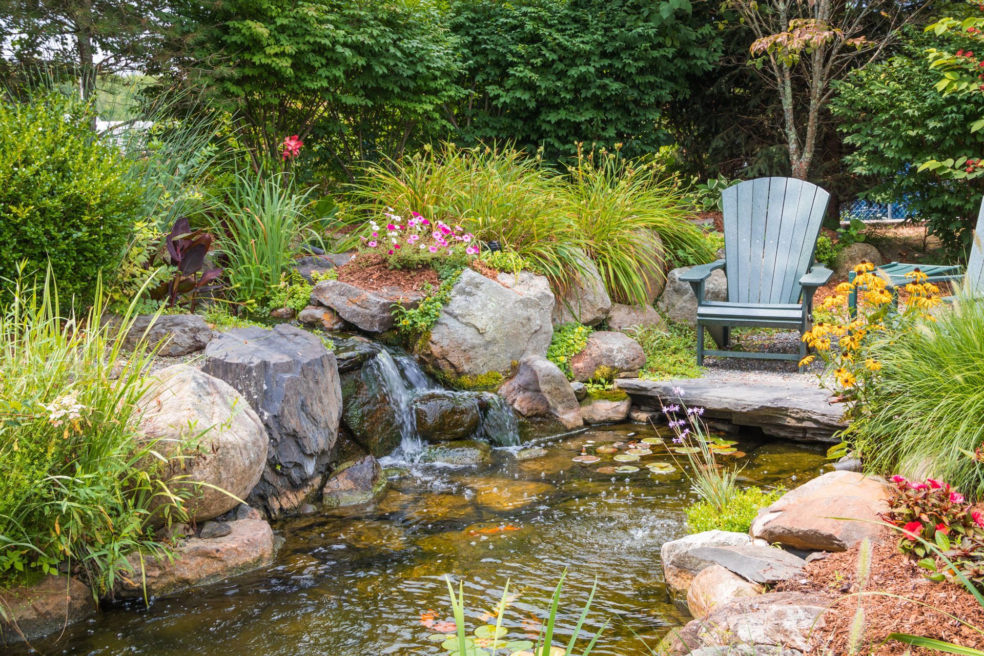 Garden pond with rocks, flowers, and a blue chair beside the water