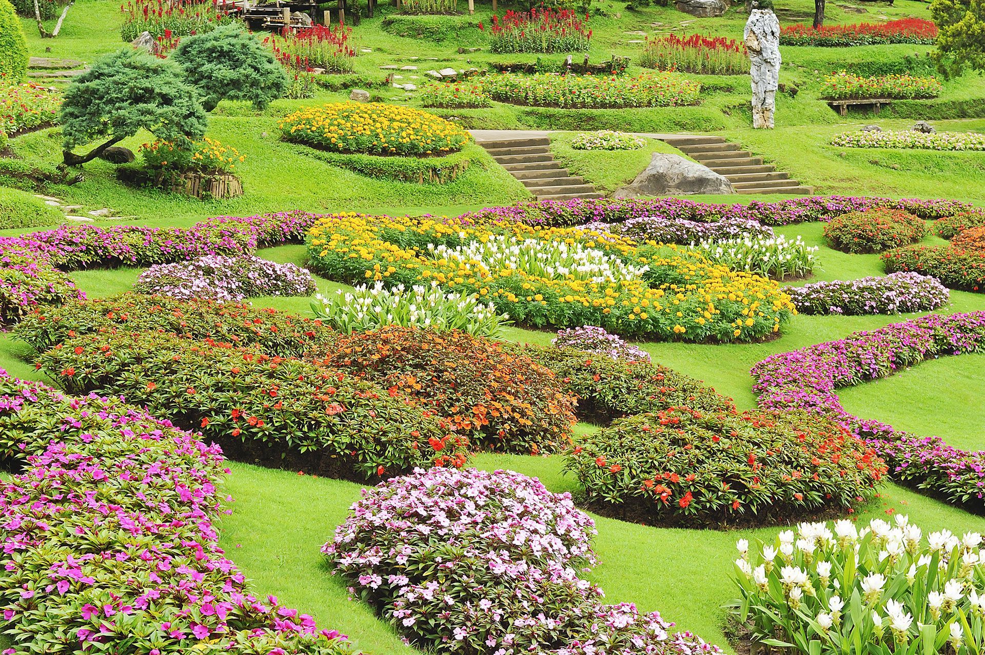 Curved garden path around a green lawn, with colorful flowers and a house in the background