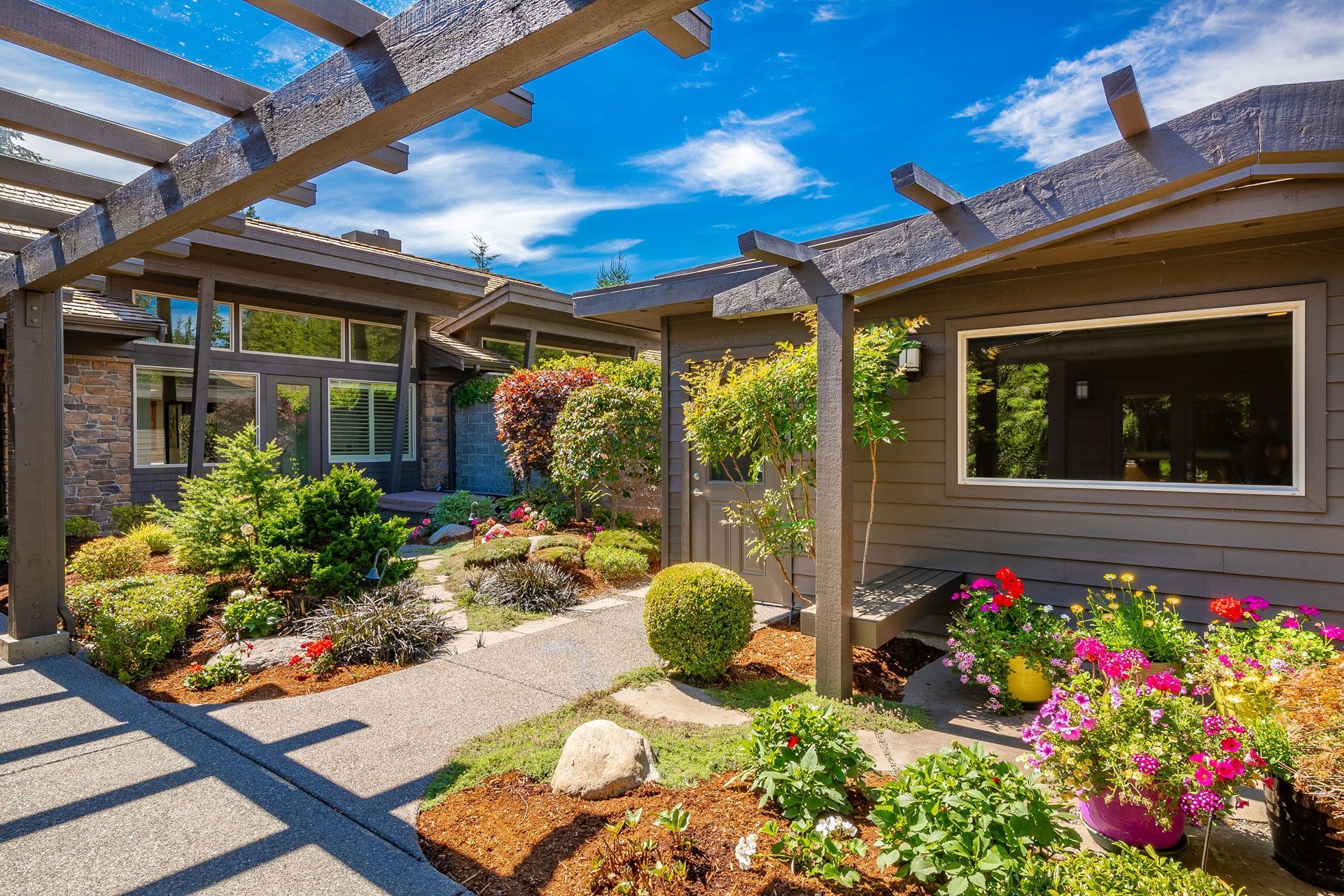 Sunny courtyard garden with pergola, stone path, and colorful flowers beside a house
