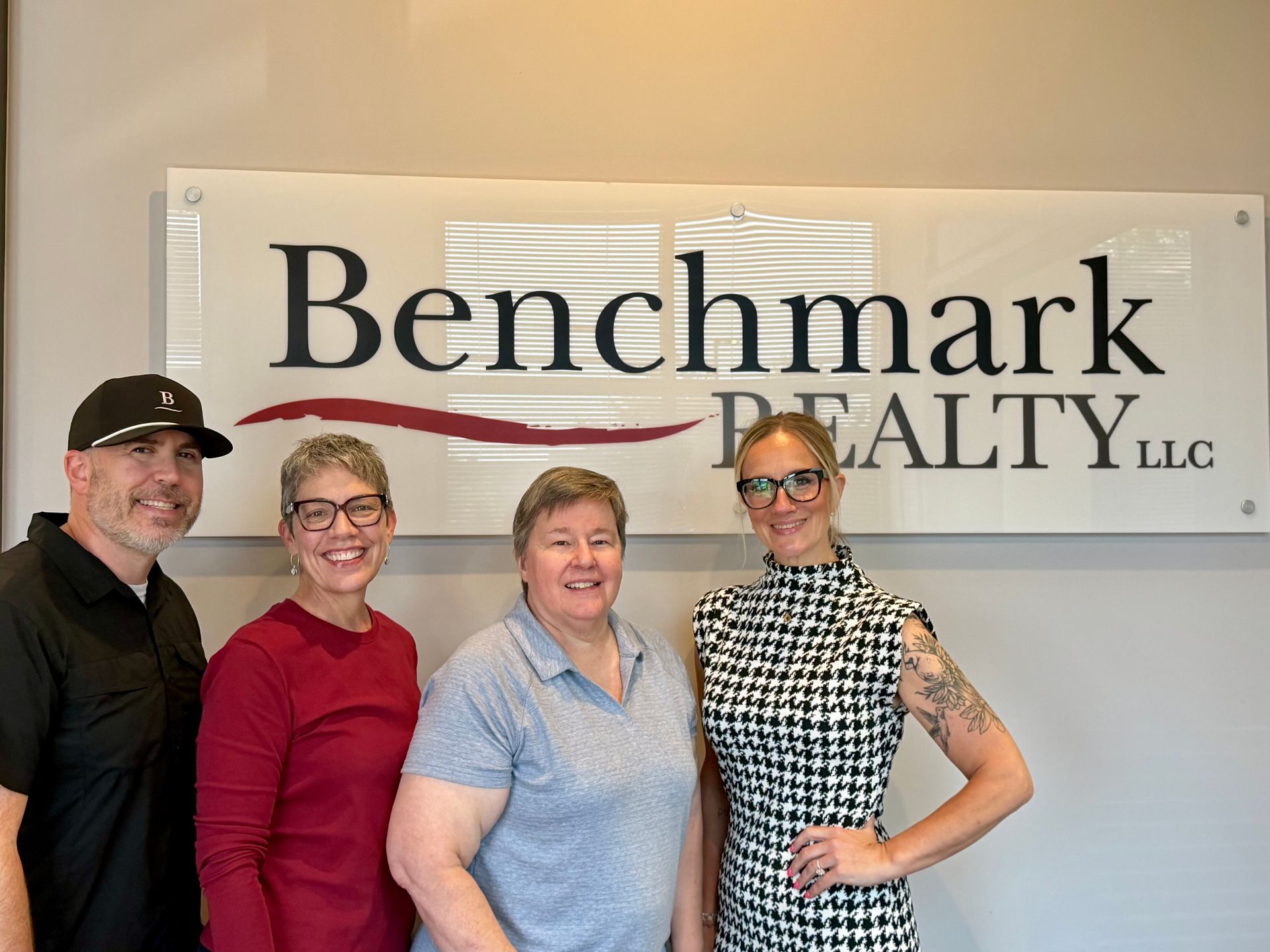 Four people smiling in front of a Benchmark Realty sign in an office lobby