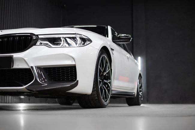 White sports sedan in a studio, front-left view, with glossy black wheels and bright headlights.