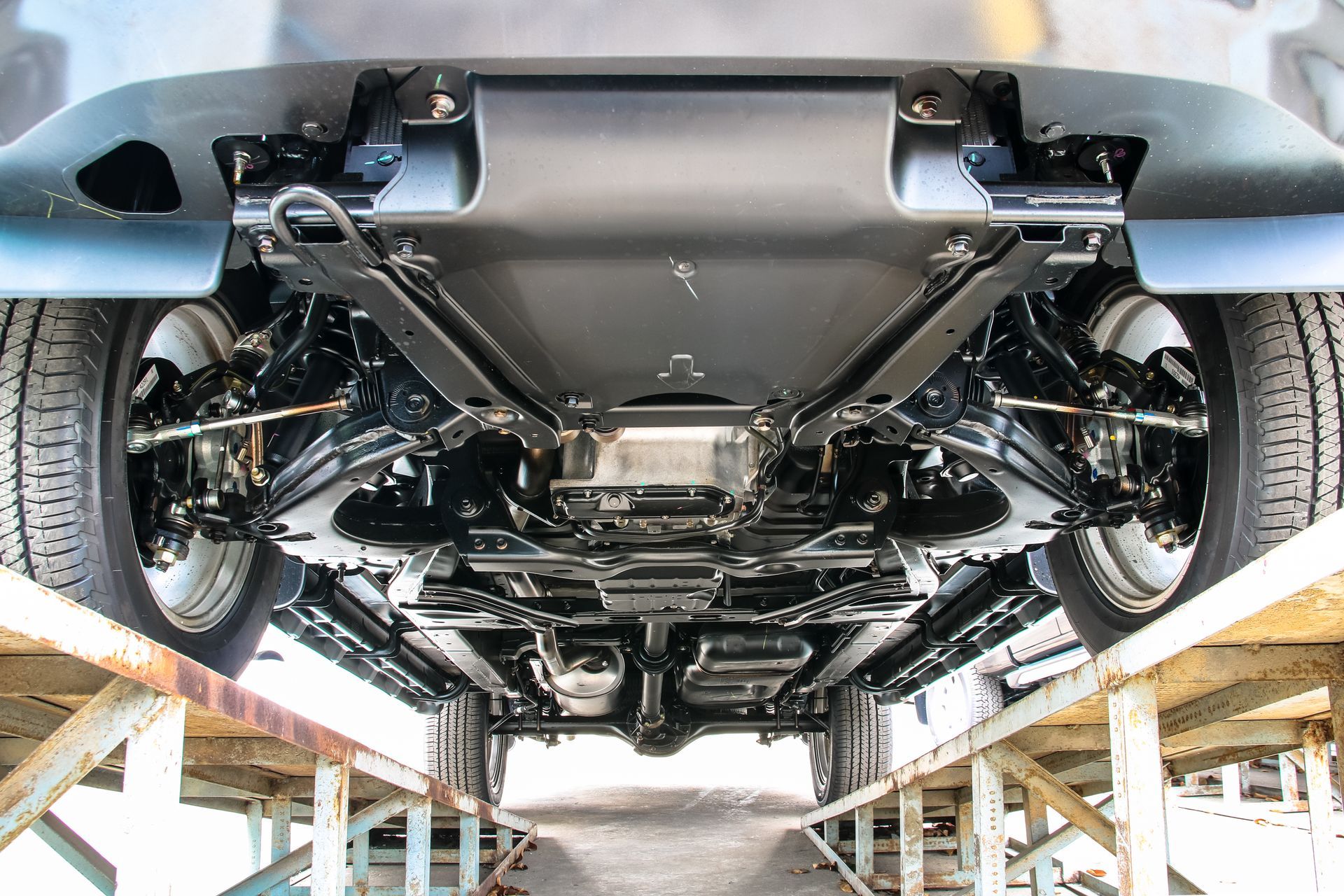 Undercarriage of a gray car on a lift, showing suspension and chassis components